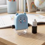 A blue elephant math roller stamp and a black ink bottle sit on a wooden desk with an open textbook and school supplies in