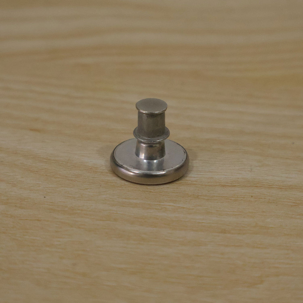 A silver metal button pin with its back lock attached, sitting on a light wooden surface.