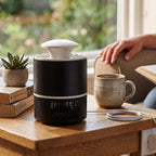 Black and white mosquito killer lamp on a wooden table next to a mug, books, and a person's hand.