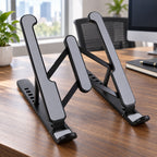 A black and gray adjustable laptop stand is positioned on a wooden desk in a bright office environment.