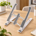 White and gray laptop stand with adjustable height and angle on a wooden desk with a plant.