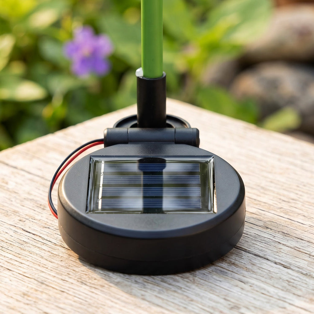 A close-up view of the black circular solar panel base of the flower stake light, resting on a wooden surface.