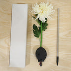 The white chrysanthemum flower solar stake light, its ground stake, and a white rectangular box laid out on a light wooden