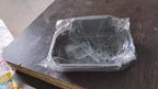 A gray self-adhesive soap dish is packaged in clear plastic on a dark brown wooden surface.
