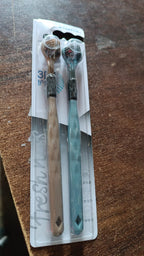 Two three-sided toothbrushes, one beige and one blue, in clear retail packaging on a wooden surface.