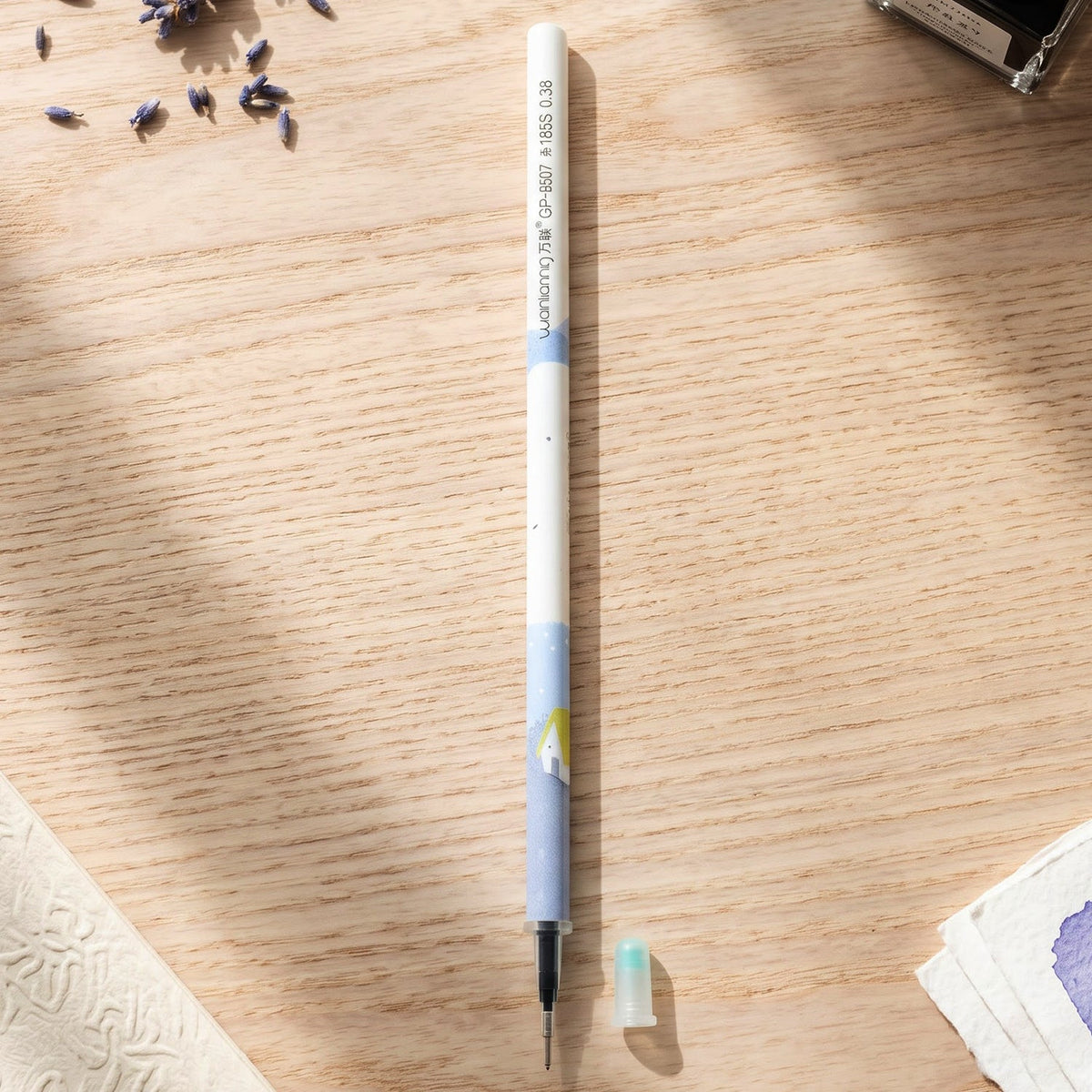 A white and blue pen refill with a small light blue cap on a wooden desk, surrounded by dried lavender.