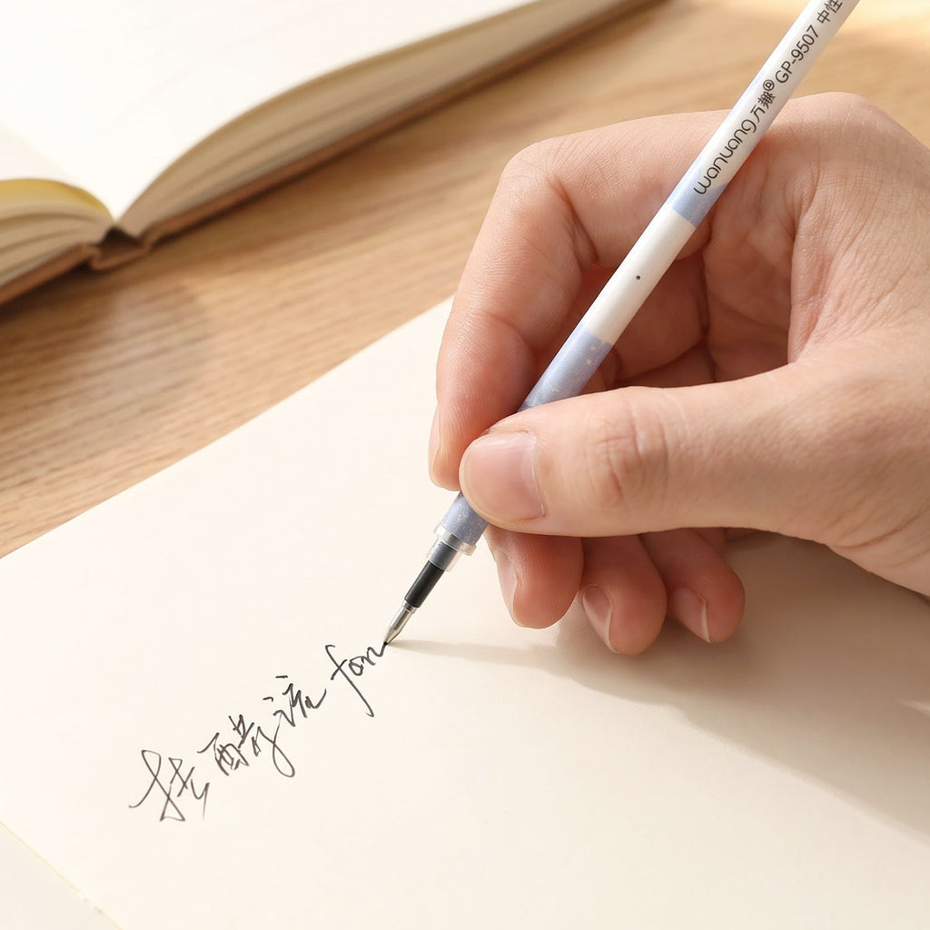 A hand writes in a foreign language on a light-colored paper with a white and blue pen refill, with a notebook.