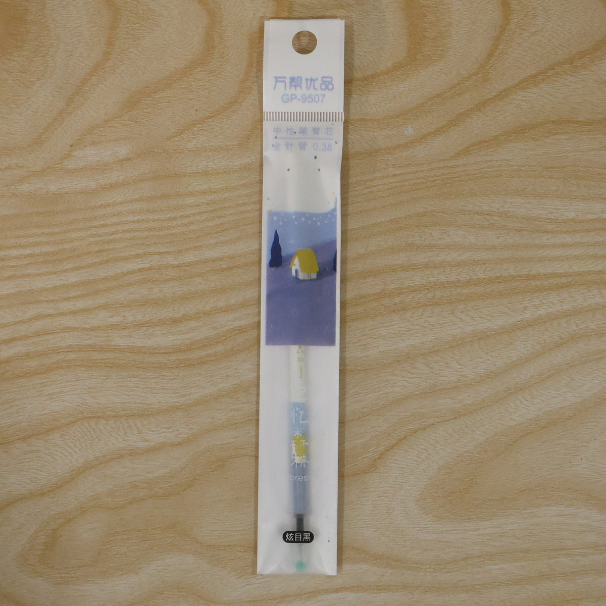 A white and blue pen refill in clear plastic packaging with a cartoon house design, lying on a wooden surface.