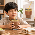 A young boy sips from an amber glass cup with a brown leather sleeve and a straw, smiling at a table.