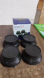 Four black round washing machine support legs are displayed in front of a blue and white product box on a wooden surface.