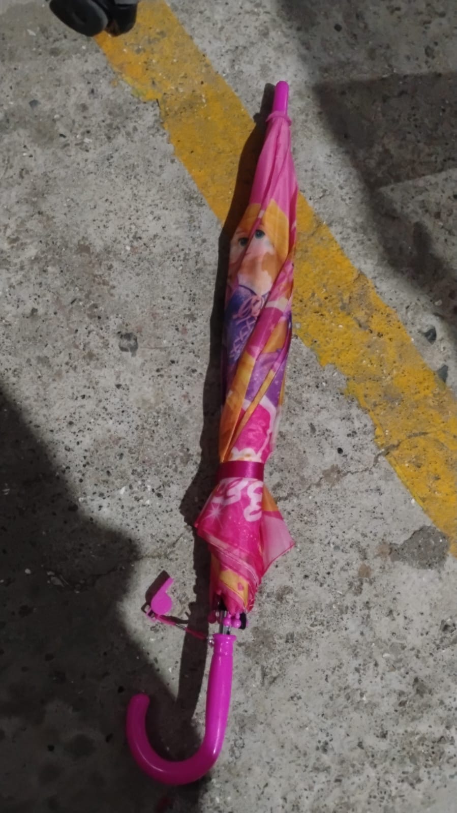 A closed pink Disney Princess umbrella with a curved handle lies on a concrete ground with a yellow line.