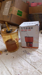 An amber glass cup with a straw and a brown sleeve sits next to its product box on a patterned surface amidst cardboard