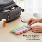 Hands place pills into the rainbow-colored organizer on a wooden table, with a travel bag in the background.