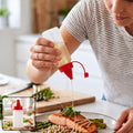 A person drizzles oil from a clear plastic squeeze bottle with a red cap onto salmon and asparagus.