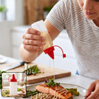 A person drizzles oil from a clear plastic squeeze bottle with a red cap onto salmon and asparagus.