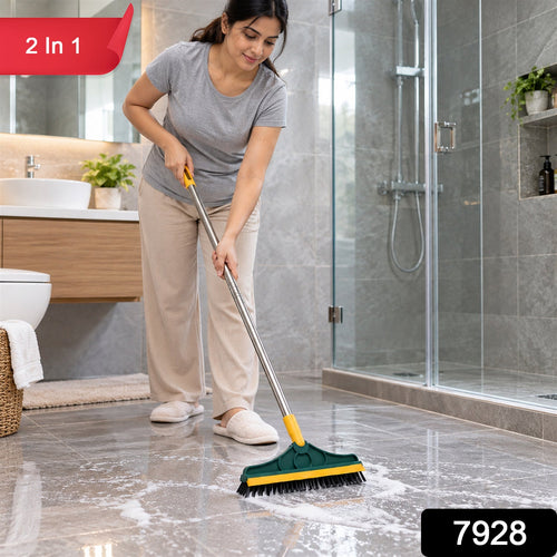 A woman in a grey shirt and beige pants scrubs a tiled bathroom floor with a green and yellow brush, creating white foam. A