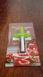 A green and silver chili corer is shown in its retail packaging on a wooden table, featuring red peppers on the card.