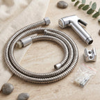 A coiled stainless steel hose, chrome bidet sprayer, wall mount, and screws on a light fabric and stone surface.
