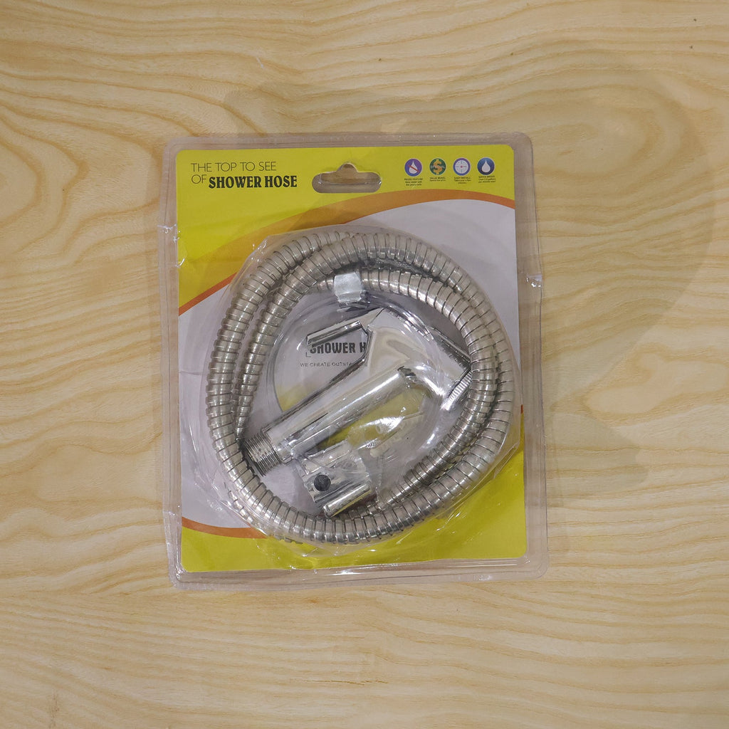 A packaged chrome bidet sprayer kit with a coiled hose is sealed in clear plastic on a light wooden surface.