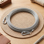 A coiled silver stainless steel wire rope with two carabiner hooks rests on a round woven mat.