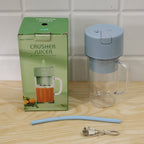 A light blue portable blender, blue straw, and USB cable are next to a green box labeled "Crusher Juicer".