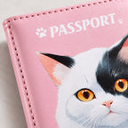 A close-up of the pink passport holder shows a detailed illustration of a black and white cat with bright yellow eyes.