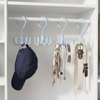 Three light blue rotating multi-hook hangers on a white closet rod, holding a navy cap, scarf, necklace, sunglasses, and a