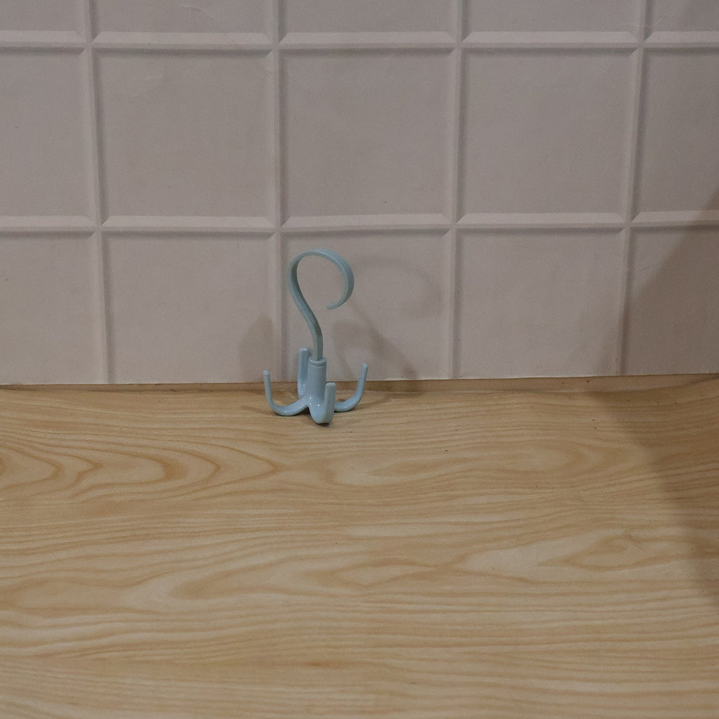 A light blue rotating multi-hook hanger sits on a light wooden surface against a white tiled wall.