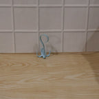 A light blue rotating multi-hook hanger sits on a light wooden surface against a white tiled wall.
