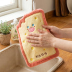A person's hands are drying on a pink-edged cartoon cheese toast microfiber towel hanging above a kitchen sink.