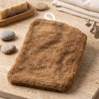 The plain brown back of a rectangular microfiber towel with a white hanging loop rests on a tiled surface with soap and