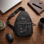 A black sling bag laid on a wooden desk with a laptop, mouse, notebook, pen, and coffee mug.