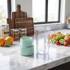 A clear blender bottle and its mint green blade base sit on a marble counter with fruits and jars of oats and nuts in the