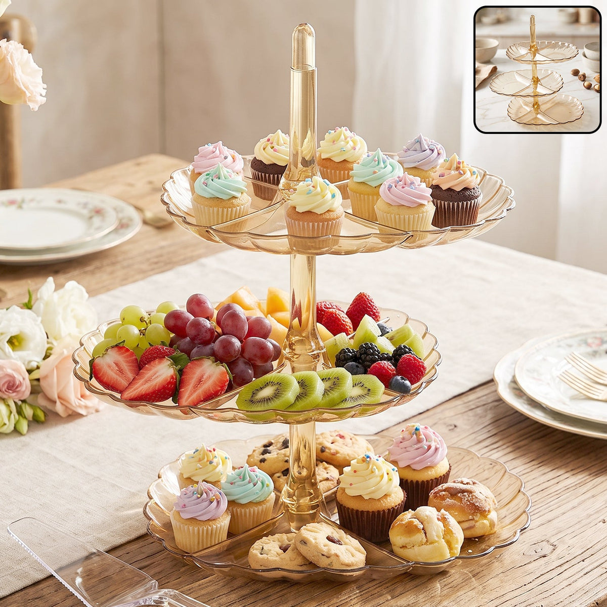 A three-tier amber acrylic serving stand holds colorful cupcakes, fresh fruit, and cookies on a wooden table.