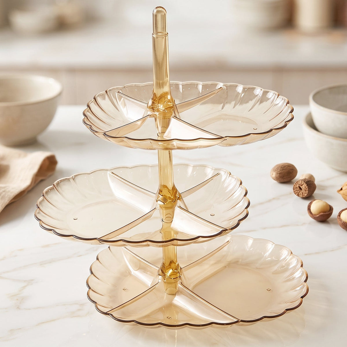 An empty three-tier amber acrylic serving stand with scalloped edges sits on a white marble surface.