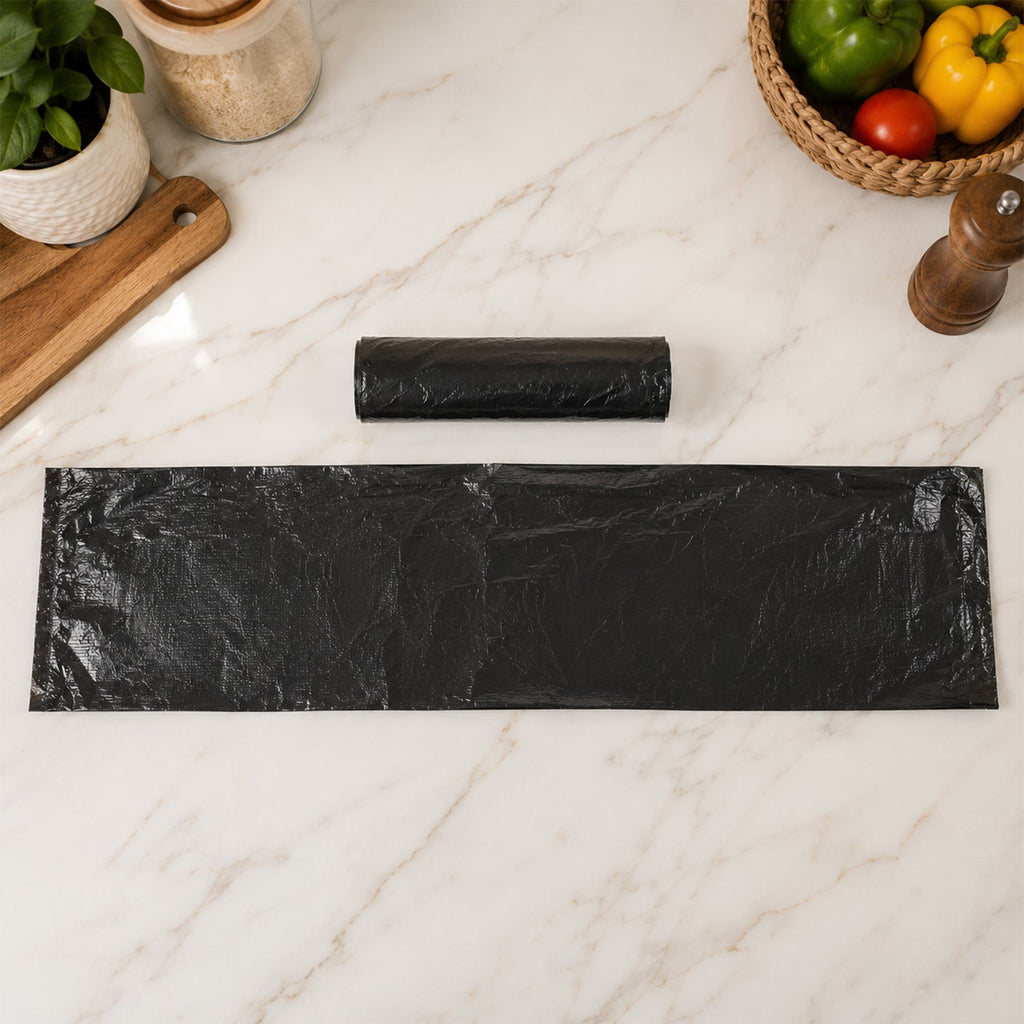 A rolled black garbage bag and a flattened bag lie on a marble counter with kitchen items in the background.
