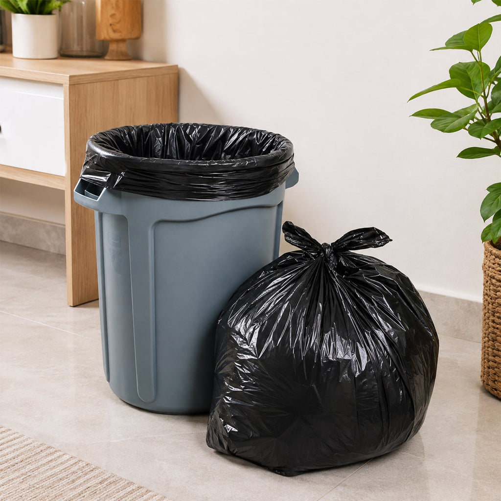 A full black garbage bag sits next to a gray trash can with a black liner, on a light gray floor.