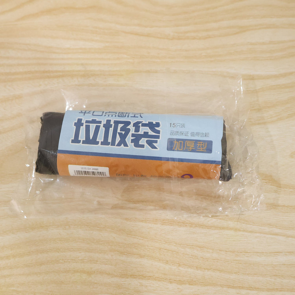 A clear plastic-wrapped roll of black garbage bags with a blue and brown label on a wooden surface.