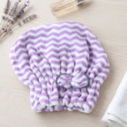 A folded purple and white chevron microfiber hair towel with a grey bow, next to lavender and a small bottle.
