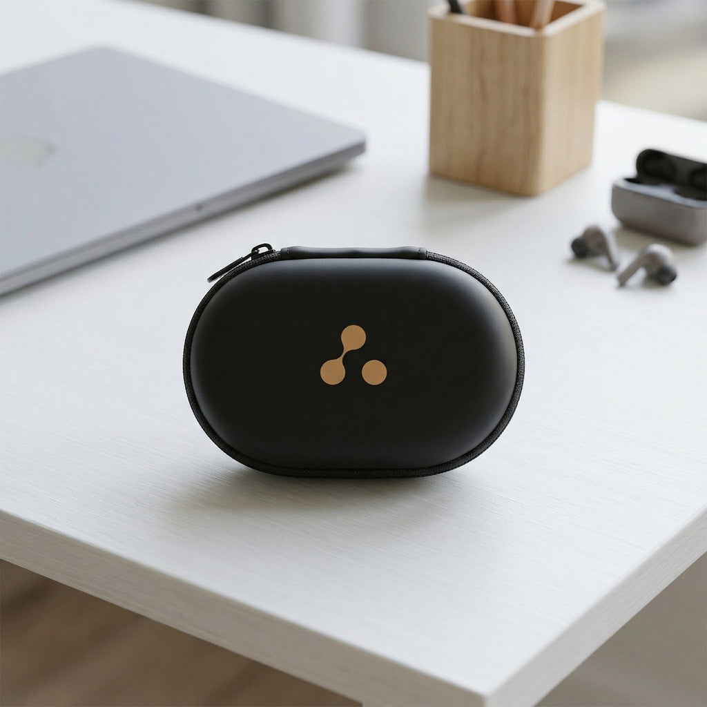 A closed black hard shell case with a gold three-dot logo sits on a white desk next to a laptop and pencil holder.