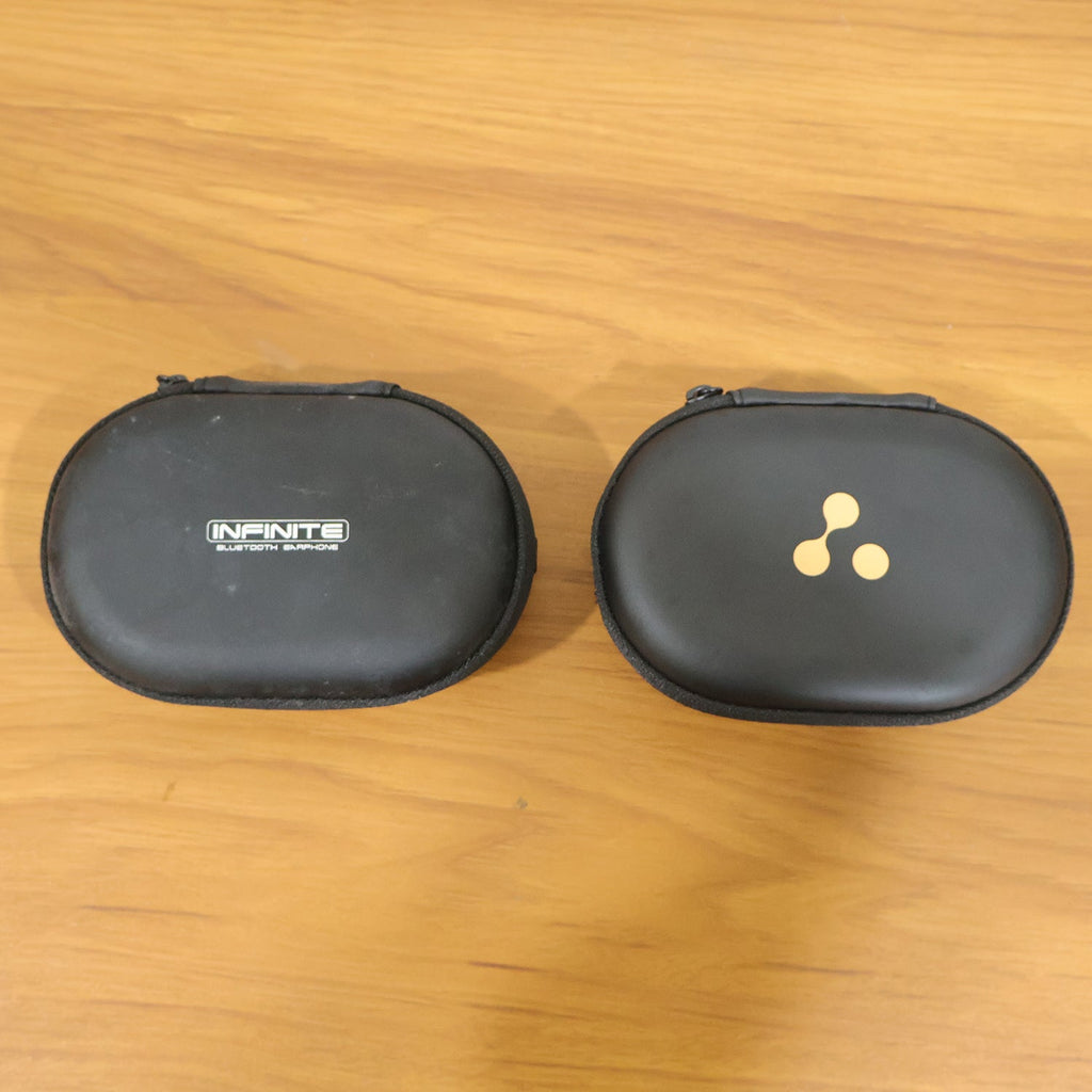 Two closed black hard shell cases are side-by-side on a wooden surface, one with a logo, the other with text.