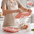 A person in an apron holds a pink ice ball tray, releasing clear ice balls into a glass bowl of fruit.