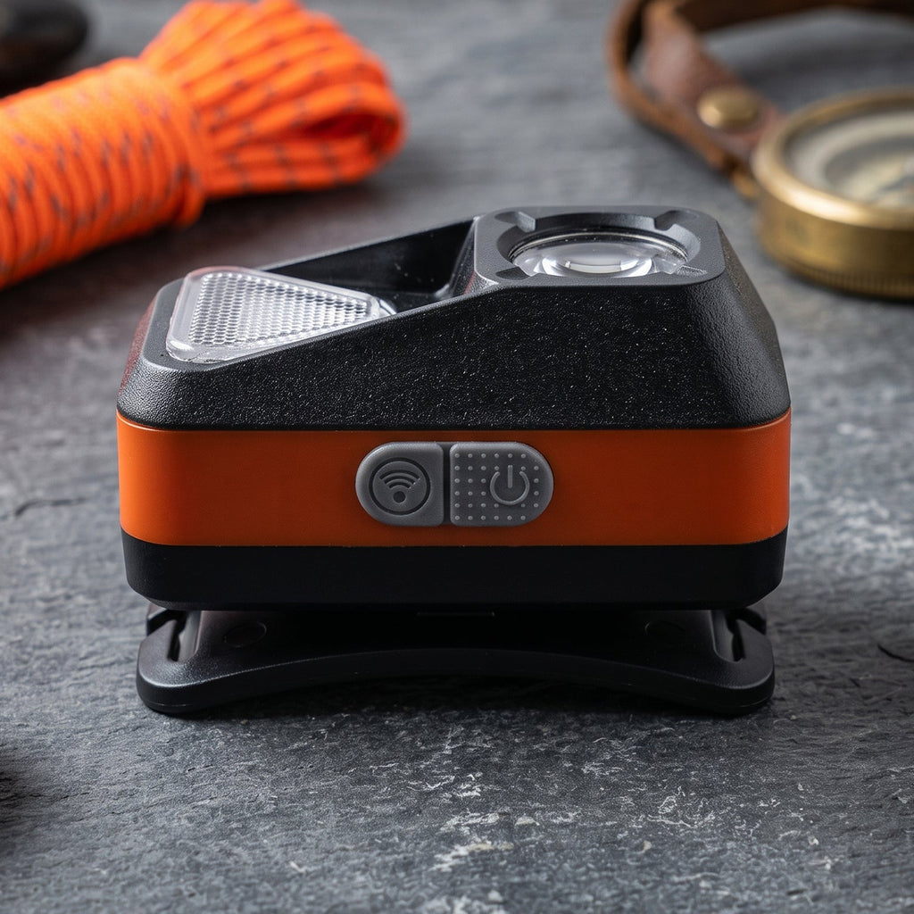 A close-up of the orange and black headlamp with control buttons, resting on a dark gray textured surface.