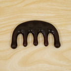 A dark brown resin scalp massager with five rounded prongs is centered on a light wooden surface.