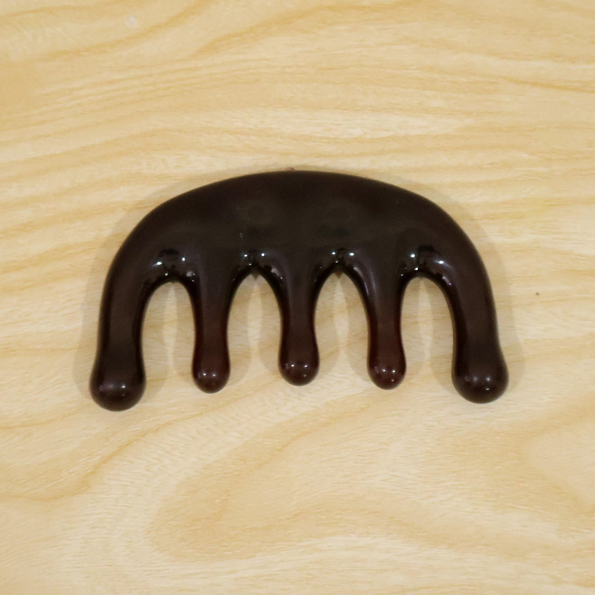 A dark brown resin scalp massager with five rounded prongs is centered on a light wooden surface.