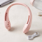 A pink portable neck fan with a white USB charging cable on a light surface with blurred background items.