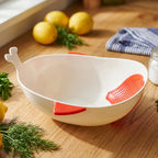 A white whale-shaped rice drainer bowl with red accents sits on a wooden counter next to lemons and fresh dill.