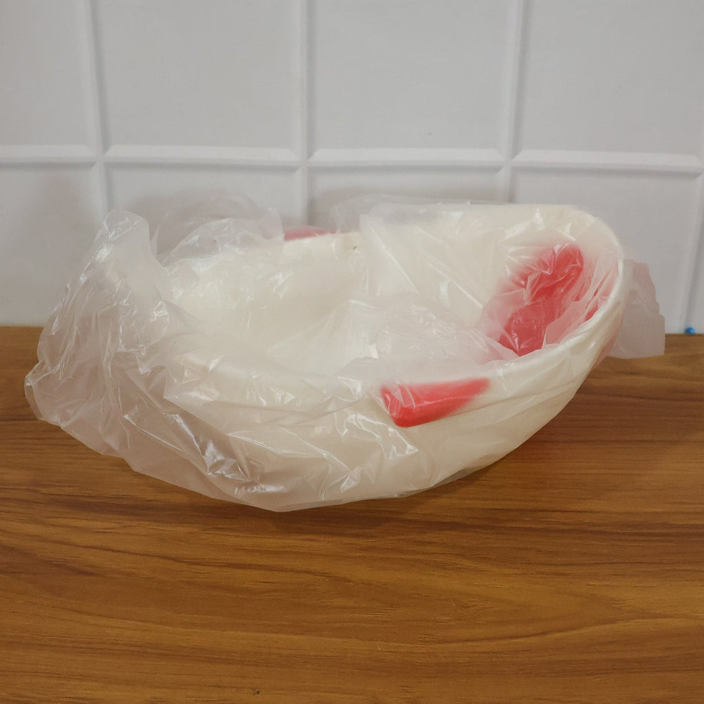 A white whale-shaped rice drainer bowl with red accents is wrapped in clear plastic packaging on a wooden surface.