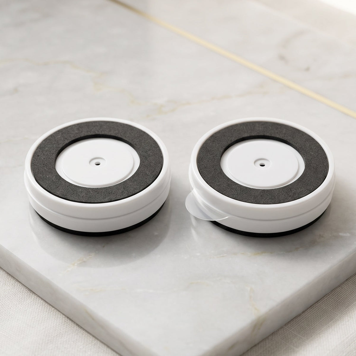 The back of two white-framed round mirrors, showing black adhesive pads, on a marble surface.