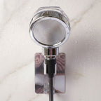 The chrome shower spray head is mounted on a wall bracket, with water droplets visible on the white marble surface.